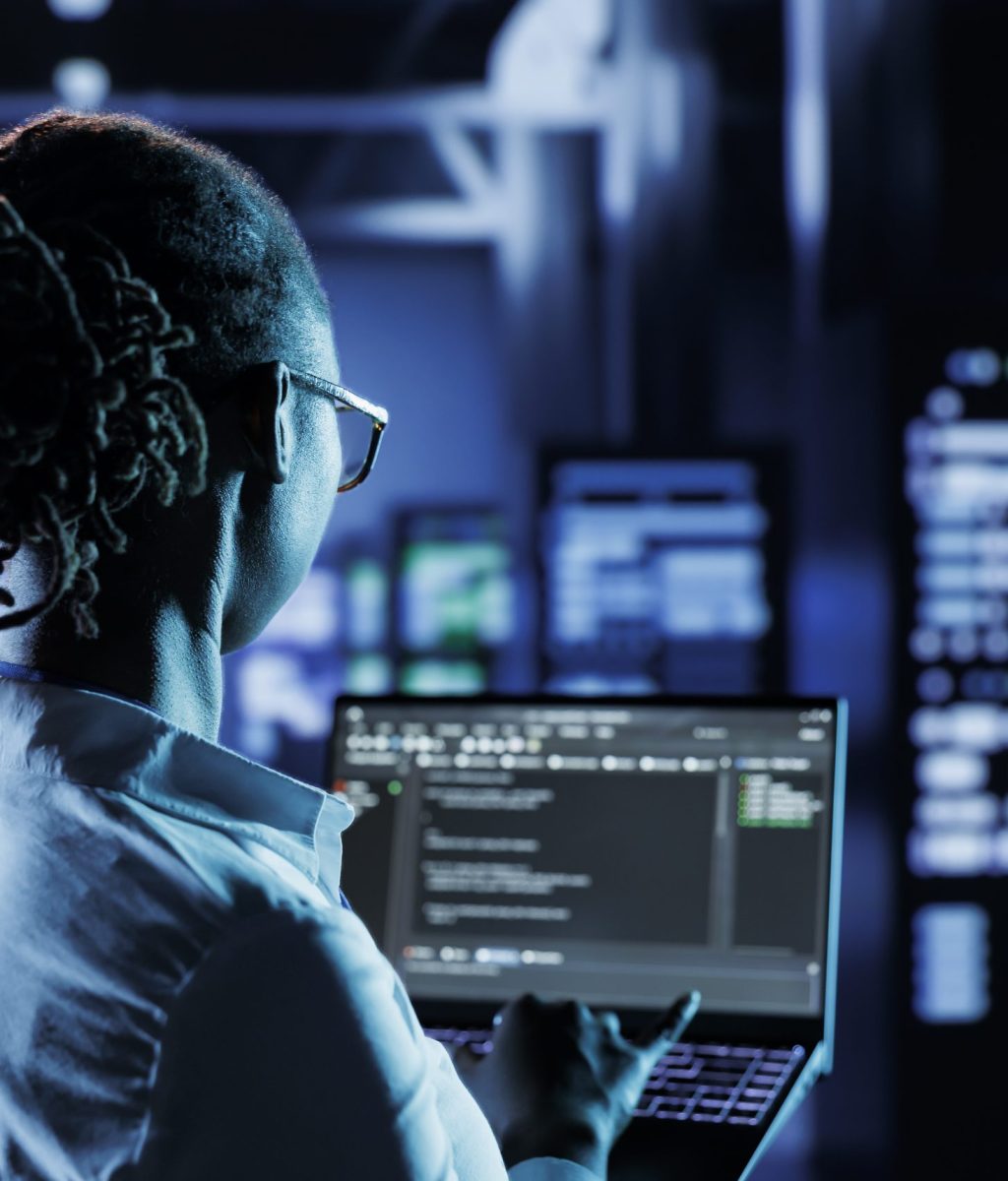 Computer scientist running code and programming on laptop, troubleshooting and upgrading high tech facility designed to accommodate multiple clusters of fully operational server rigs