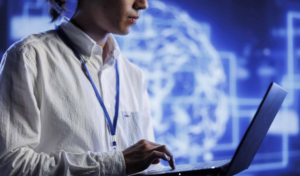System administrator using laptop to maintenance artificial intelligence neural networks simulating human thought processes in computerized model. Adept professional doing checkup on AI systems