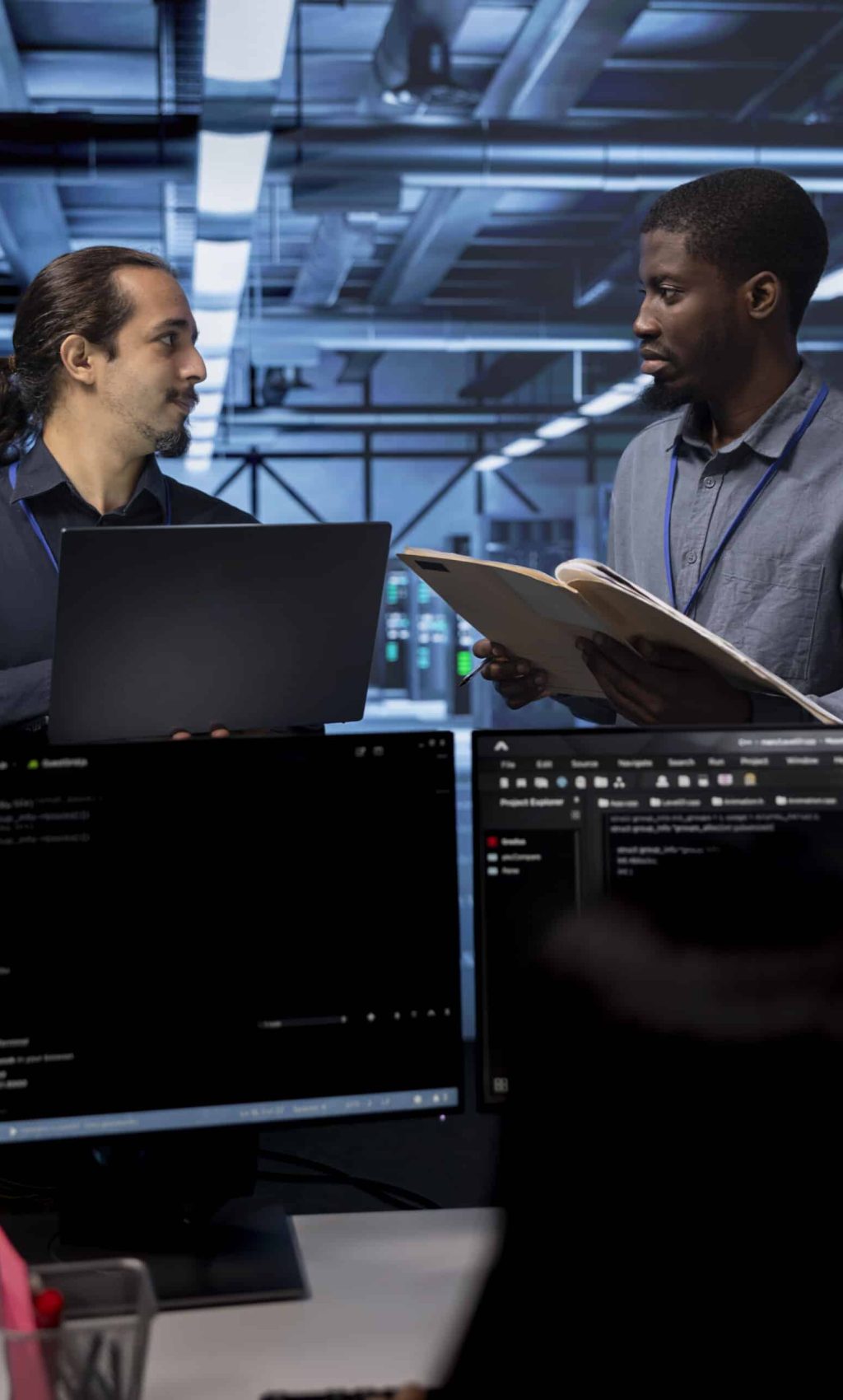 Manager getting feedback from engineer while overseeing data center, looking for firewall misconfigurations. Supervisor talking with workers in server room, asking about systems bottlenecks